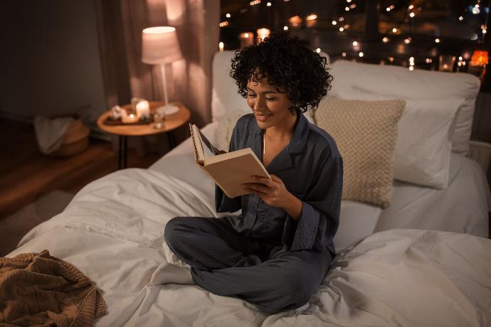 Femme détendue qui lit en pyjama assise dans son lit