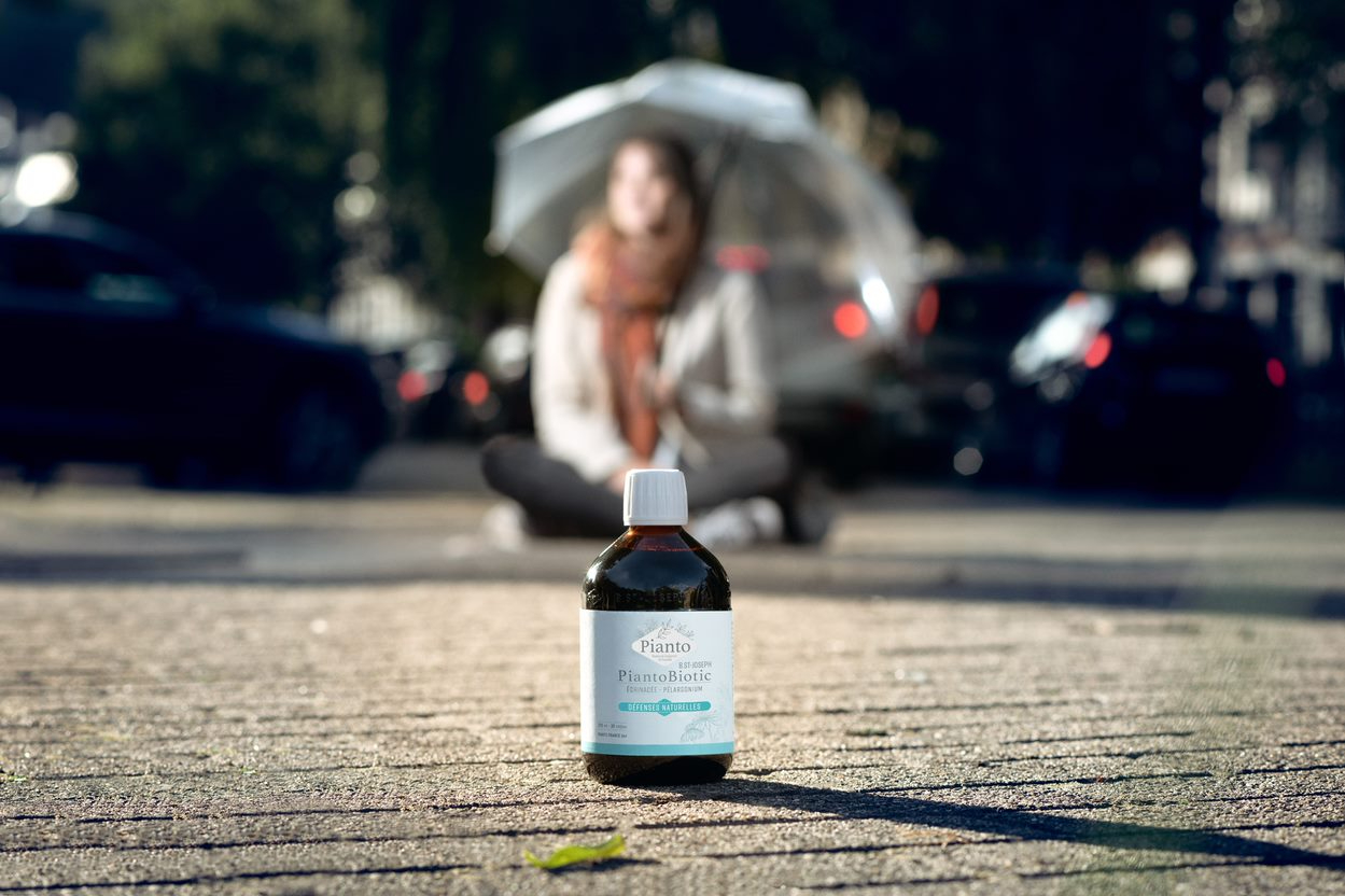 Flacon de PiantoBiotic DEFENSES NATURELLES avec en arrière plan une  jeune femme sous un parapluie