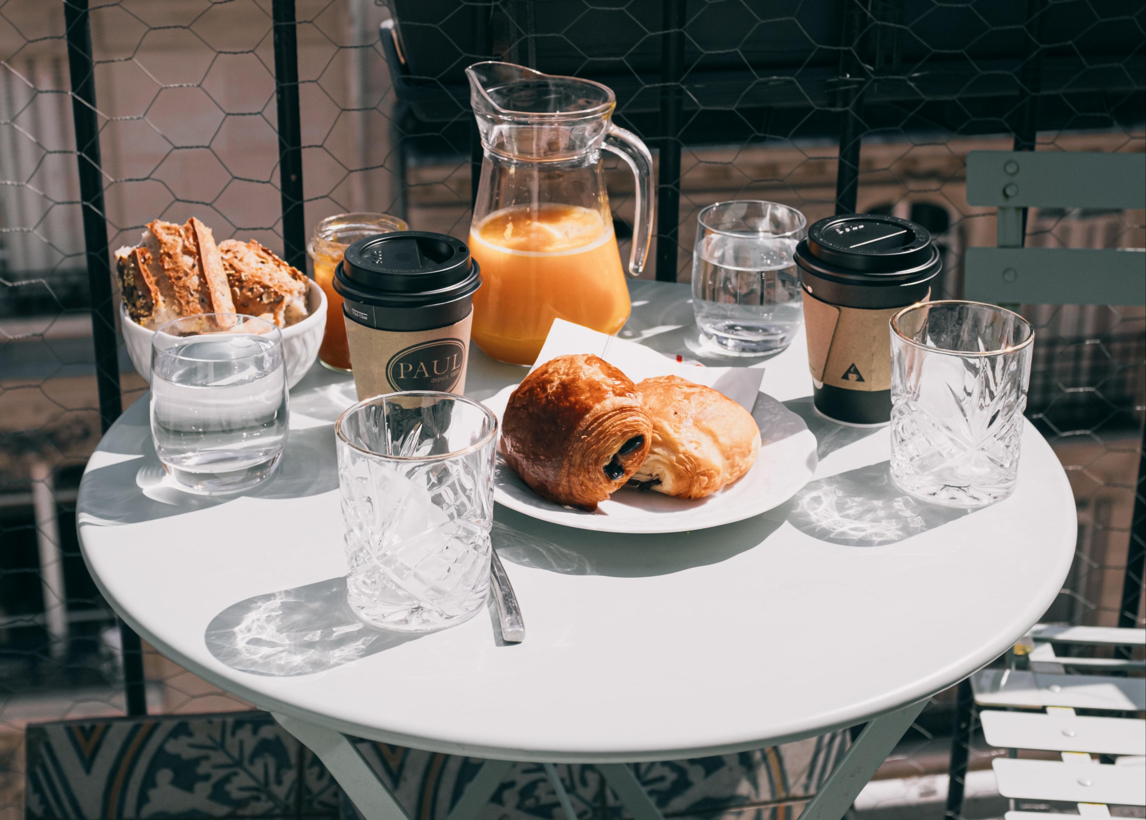 Table ensoleillée avec un petit déjeuner comportant des viennoiseries, du jus d'orange et des cafés pour deux personnes 