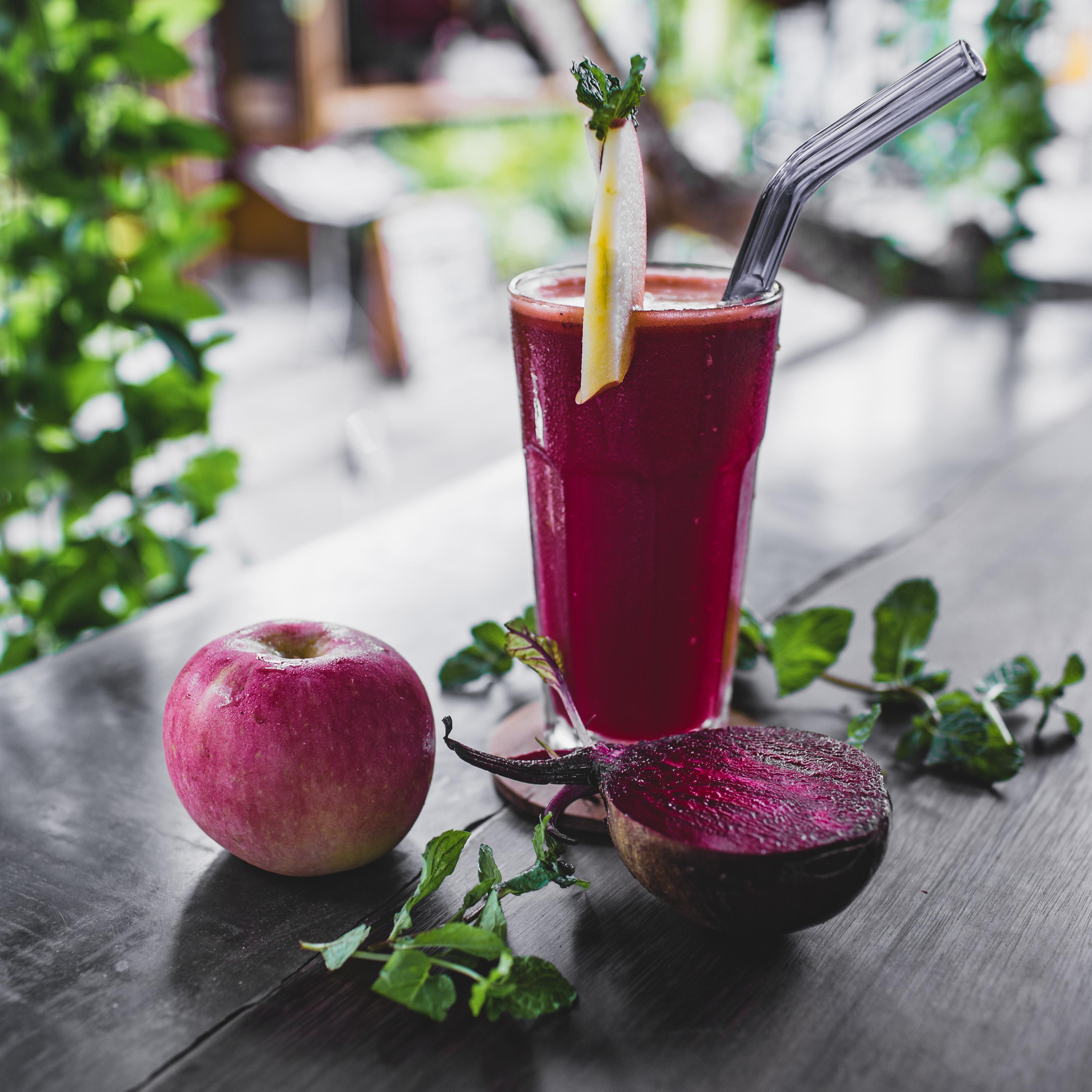 Verre de jus  posé sur une table à côté d'une pomme et d'une demi betterave  